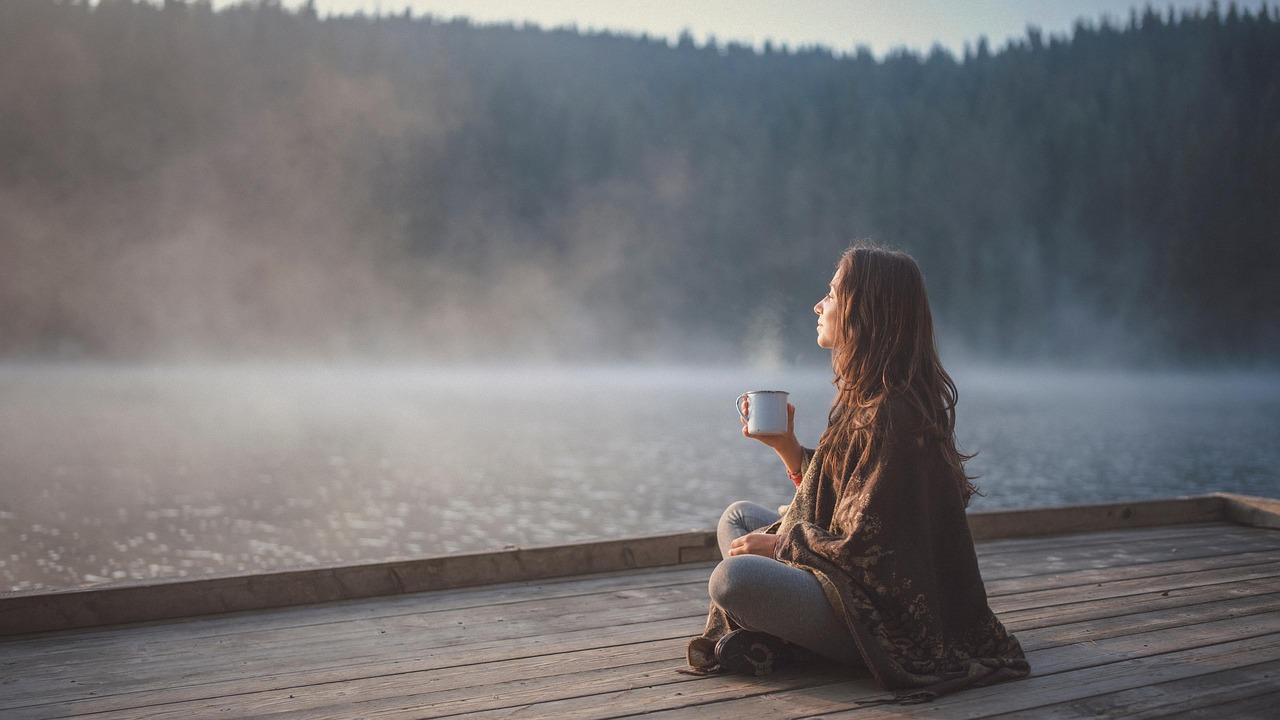 Contemplative woman drinking coffee on a dock near wtaer